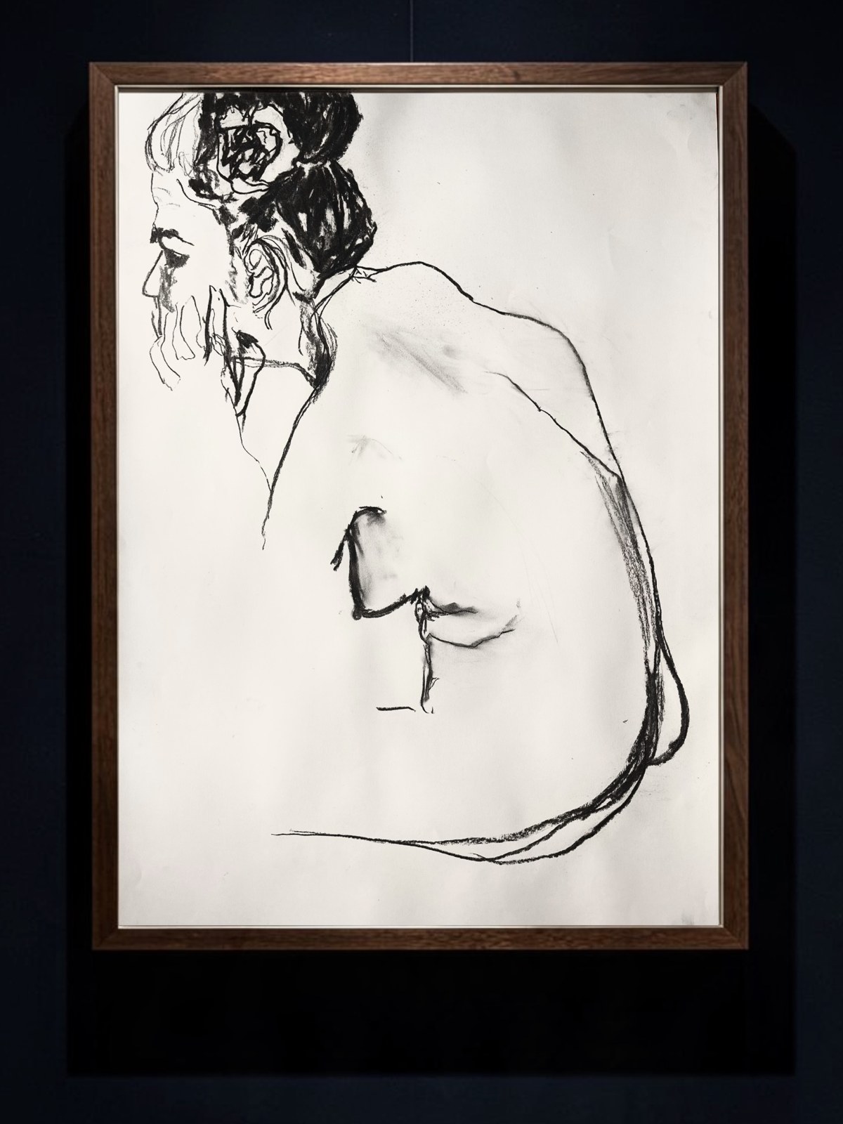 A charcoal drawing of a seated, bearded figure seen in profile from behind, in a walnut frame on a deep navy wall